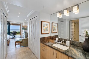 A modern bathroom with a large mirror, marble countertop, and wooden cabinets. - Oceanfront Retreat with Panoramic Views & Beachfront Lanai -Mahana (Lahaina)