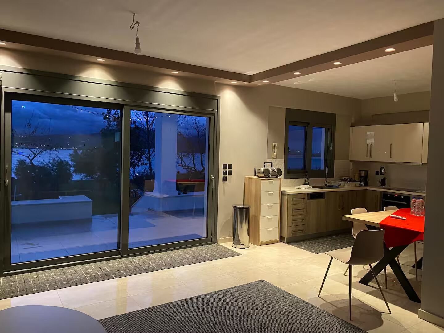 A modern kitchen with sliding glass doors, a dining area with a red table, and a view of the outdoors.