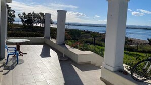 A terrace with a table and chairs, white pillars, and a view of the sea. - Beach View House with Private Garden (ΧΑΛΚΙΔΑ)
