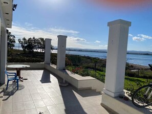 Eine Terrasse mit Tisch und Stühlen, weißen Säulen und Meerblick.