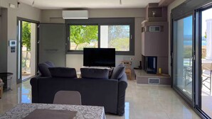 A modern living room with a flat-screen TV, a sofa, a dining table, and a fireplace. - Beach View House with Private Garden (ΧΑΛΚΙΔΑ)