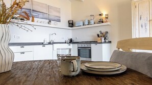 Moderni keittiö, jossa on valkoiset kaapit, puinen ruokapöytä ja maljakko, jossa on kuivattuja kasveja.