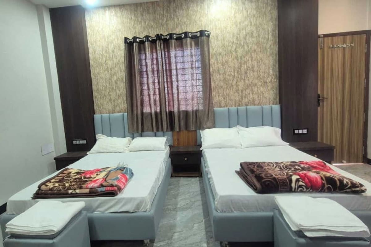 Habitación de hotel con dos camas individuales, un ventanal con cortinas, un armario y una mesita de noche.