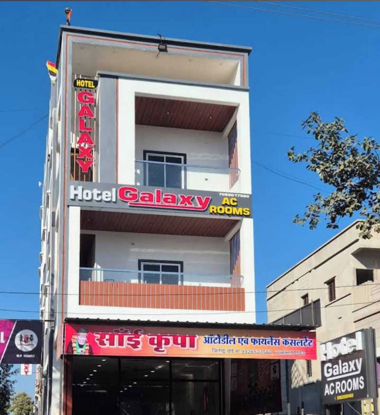 Un edificio de varios pisos con un cartel que dice 'Hotel Galaxy AC Rooms' en el segundo piso.