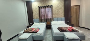 Habitación de hotel con dos camas individuales, un ventanal con cortinas, un armario de madera y suelo alfombrado.
