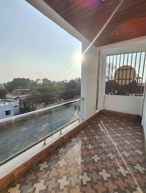 Un balcón con suelo estampado, baranda de vidrio y vistas a una calle y edificios.