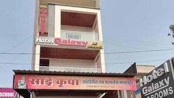 A two-story building with a sign for 'Hotel Galaxy AC Rooms' and another sign for 'Sain Kupa' with contact information.