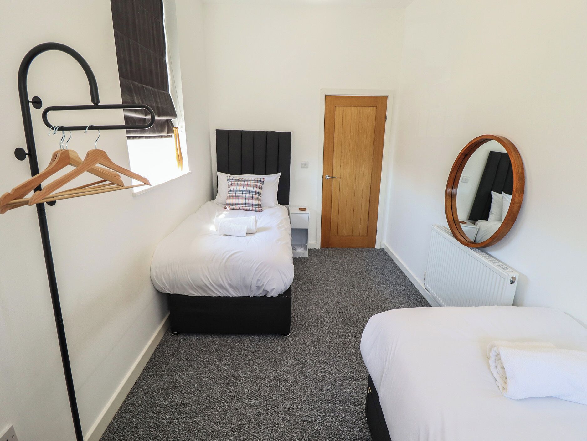 A bedroom with a bed, a dresser, a mirror, a coat rack, and a door.