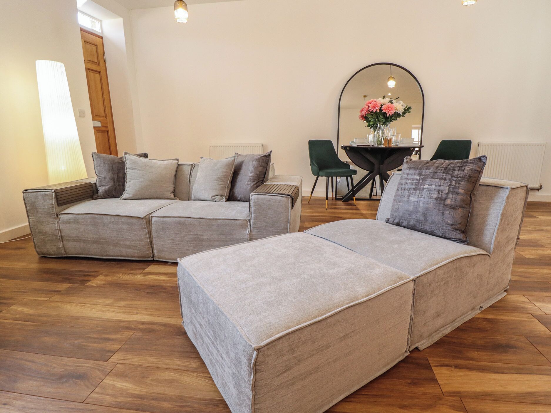 Ein modernes Wohnzimmer mit einer Eckcouch, einem Esstisch mit Stühlen und einem großen Spiegel.