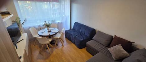 A compact living space with a dining table, chairs, a sofa, and a television.