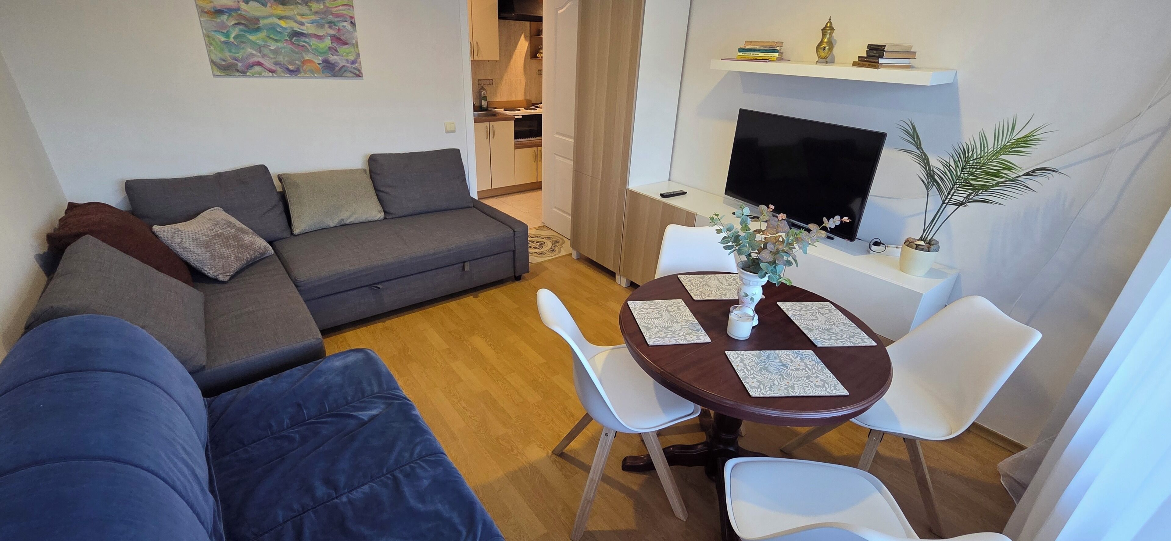 Un espace de vie compact comprenant un canapé, une table à manger avec des chaises, un téléviseur et un petit coin cuisine.