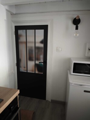 Ett kompakt kök med en svart dörr, en vit mikrovågsugn och en lampa på väggen.