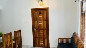 A room with a wooden door, a ceiling fan, a light fixture, a dining table with chairs, and a sofa.