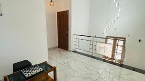 A spacious room with a chess table, a hanging light fixture, and a balcony with a railing.