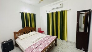 A bedroom with a bed, a wooden headboard, a red chair, a wardrobe, a ceiling fan, and a wall-mounted air conditioner.