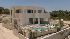 A modern two-story house with a swimming pool, outdoor seating, and a stone retaining wall. - Norma Villa, Heated Pool, Walk to Shops & Dining (Rethymno)
