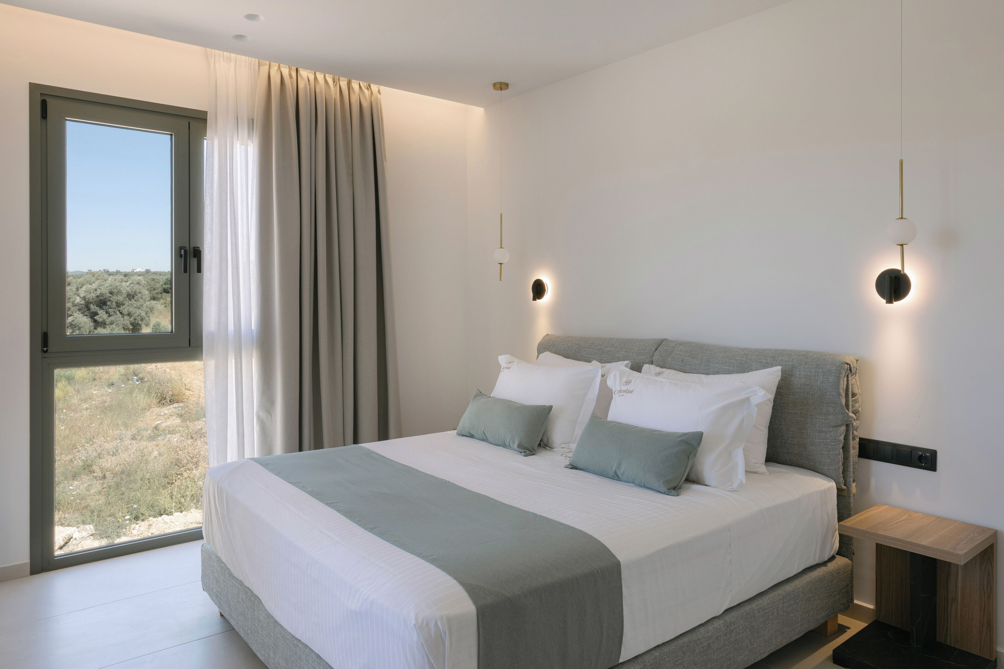 A modern bedroom with a large bed, a view through a window, and a nightstand with a lamp.