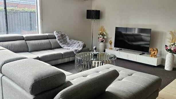 Ein modernes Wohnzimmer mit einem Ecksofa, einem Flachbildfernseher, einem Couchtisch und einer dekorativen Vase.