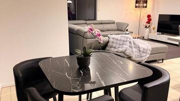 Un salon moderne avec un coin repas, comprenant une table et des chaises en marbre noir, un canapé gris et un téléviseur à écran plat.