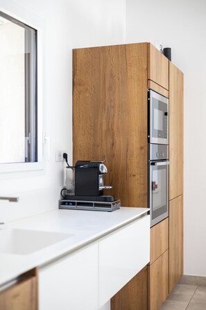 A modern kitchen with a built-in oven, a coffee machine, and a window. - Villa L'Aparté Beauvallon | Pool, Movie Theater, Fitness Center & Golf (GRIMAUD)