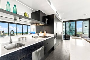 A modern kitchen with a large island, stainless steel appliances, and a view of the city. - Luxury CBD Top Floor Apt w/Gym spa pool n Car Spot (Southbank)