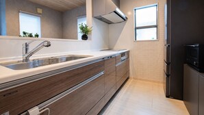 A modern kitchen with a stainless steel sink, wooden cabinets, a black refrigerator, and a window providing natural light. - Fuji Terrace -EIRAN- (Gotemba)