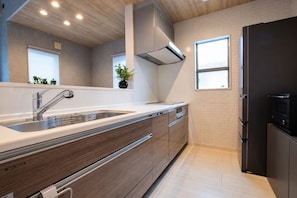 A modern kitchen with a stainless steel sink, wooden cabinets, a black refrigerator, and a window providing natural light. - Fuji Terrace -EIRAN- (Gotemba)