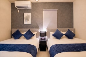 Quarto de hotel com duas camas, uma mesa de cabeceira com abajur, ar condicionado e um quadro na parede.