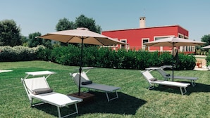 A well-maintained lawn with multiple lounge chairs and umbrellas, a red building in the background, and a clear sky. - Appartamento Sea - Tenuta Fascianello (Puglia)