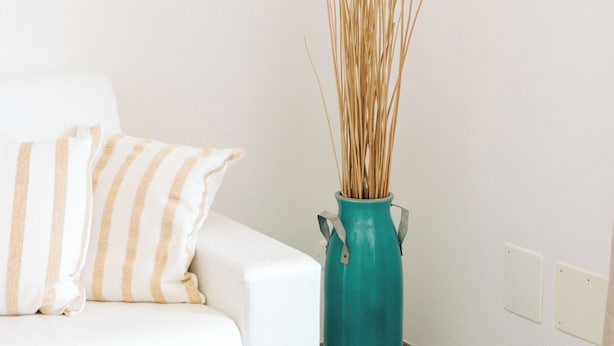 A white sofa with striped pillows, a teal vase with tall, thin plants, and a woven stool. - Appartamento Sea - Tenuta Fascianello (Puglia)
