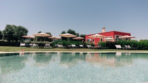 A pool area with lounge chairs and umbrellas, a red building in the background, and clear skies. - Appartamento Sea - Tenuta Fascianello (Puglia)