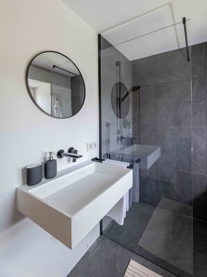Ein modernes Badezimmer mit einem weißen Waschbecken, einem runden Spiegel und einer Duschkabine aus Glas.