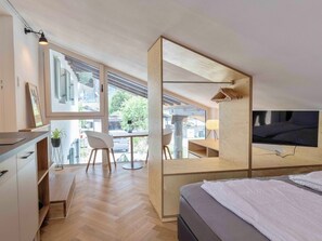 A modern bedroom with a bed, a TV, and a desk area with a chair and a plant. - Gletschergarten Vacation Rental (Auerbach)