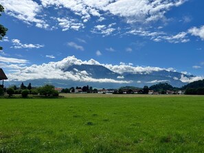 Ländliche Landschaft mit einem Berg im Hintergrund, einem grünen Feld im Vordergrund und mehreren Häusern.