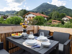 Ein Essbereich mit einem für zwei Personen gedecktem Tisch, umgeben von Korbstühlen, mit Blick auf Berge.
