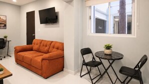 A modern living room with a sofa, a TV mounted on the wall, a dining table with chairs, and a window with a view of a building. - Hotel Boutique Venecia CDMX (Mexico City)