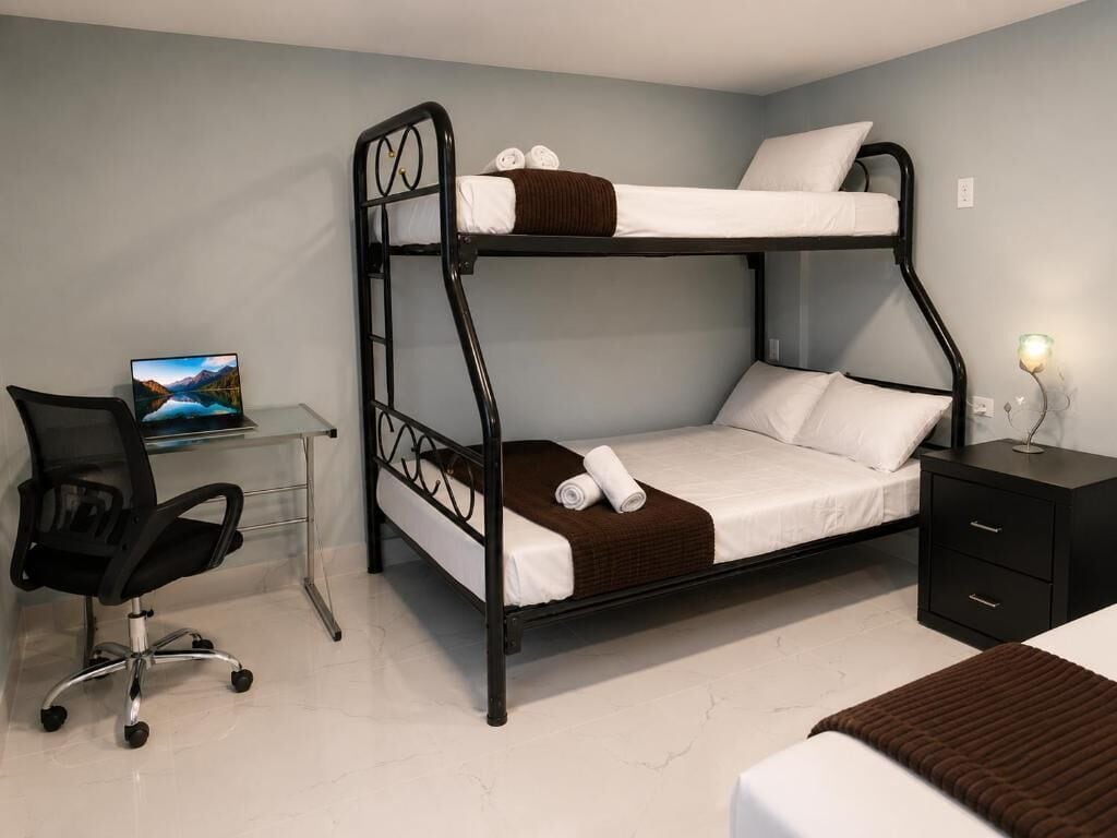 A bunk bed with a desk and chair, a bedside table with a lamp, and a painting on the wall.