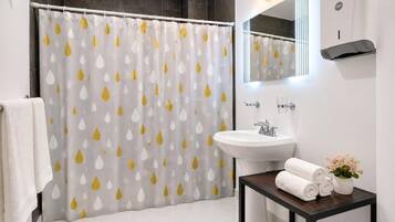 Un baño con cortina de ducha, lavamanos, espejo y una mesita con toallas y flores.