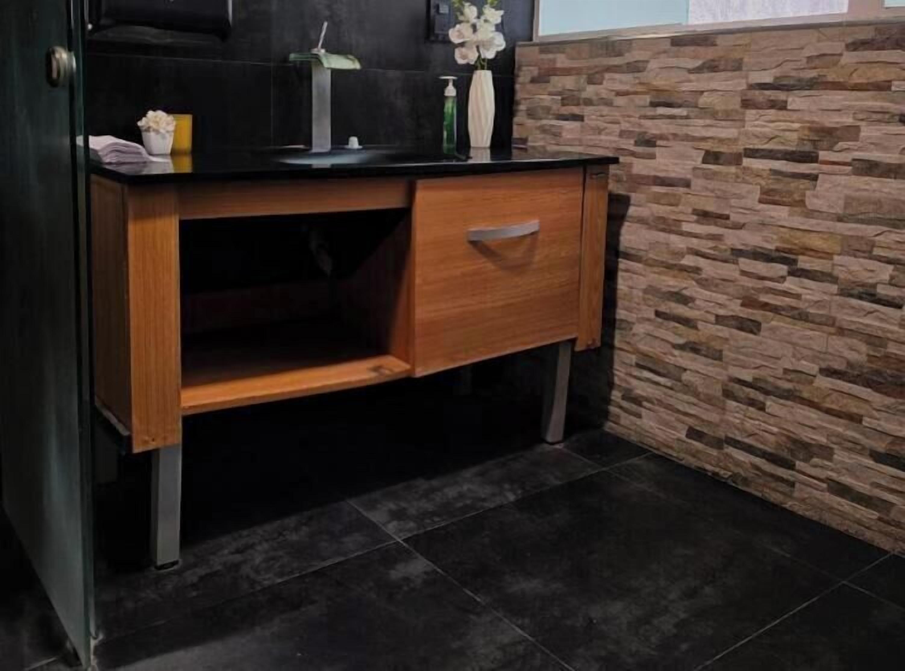 Ein Holztisch mit Schublade, einer schwarzen Arbeitsplatte und einer Blumenvase.