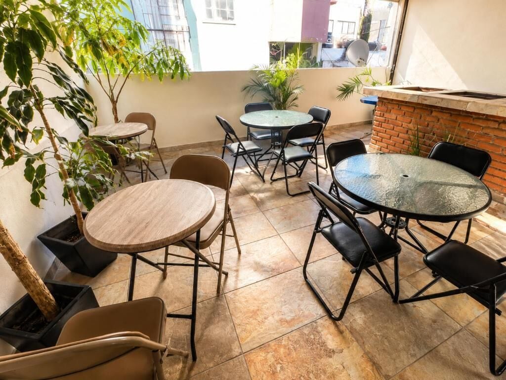 Un patio con mesas y sillas redondas, plantas en macetas y un muro de ladrillo.