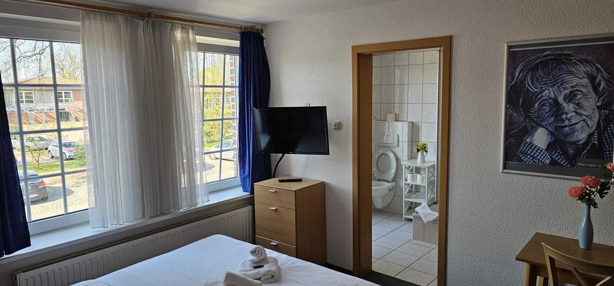 Habitación de hotel con cama, televisor, espejo, baño y vista al exterior.