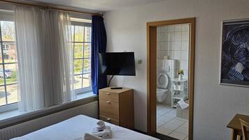 Habitación de hotel con cama, televisor, espejo, baño y vista al exterior.