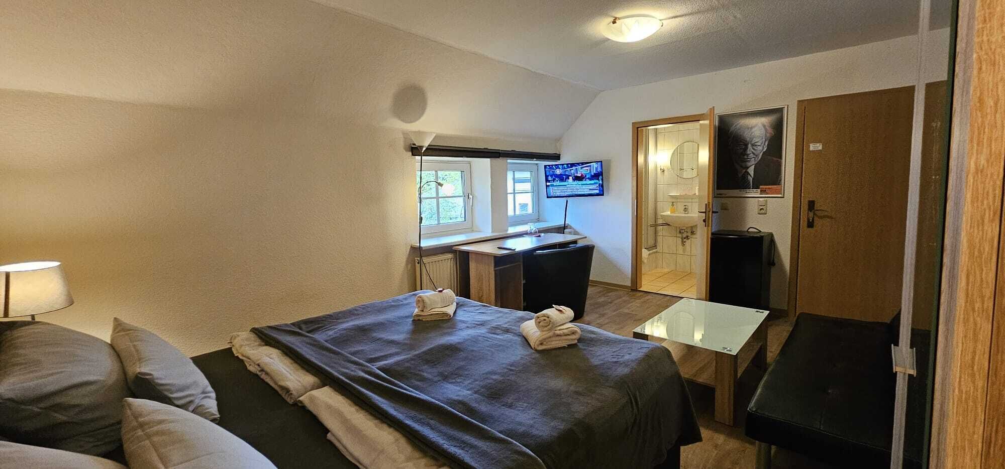 Ein Hotelzimmer mit Bett, Schreibtisch, Fernseher, Spiegel und Badezimmer.