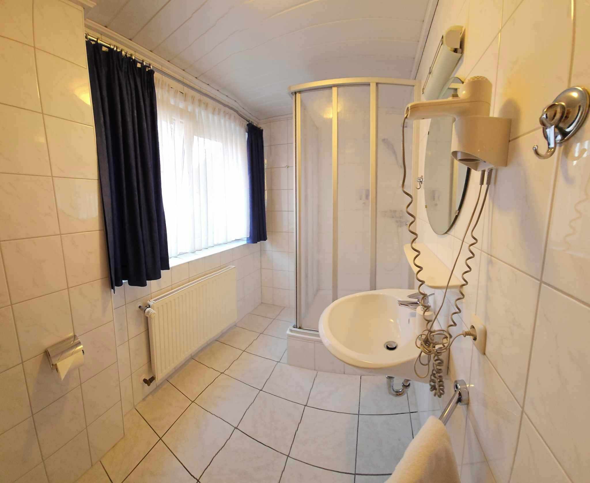 Ein Badezimmer mit Waschbecken, Spiegel, Handtuchhalter, Dusche und einem fenster mit Vorhängen.