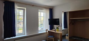 A room with two windows, a desk with a computer, a chair, and a television. - Tropicana Lüneburger Hof (Munster im Heidekreis)