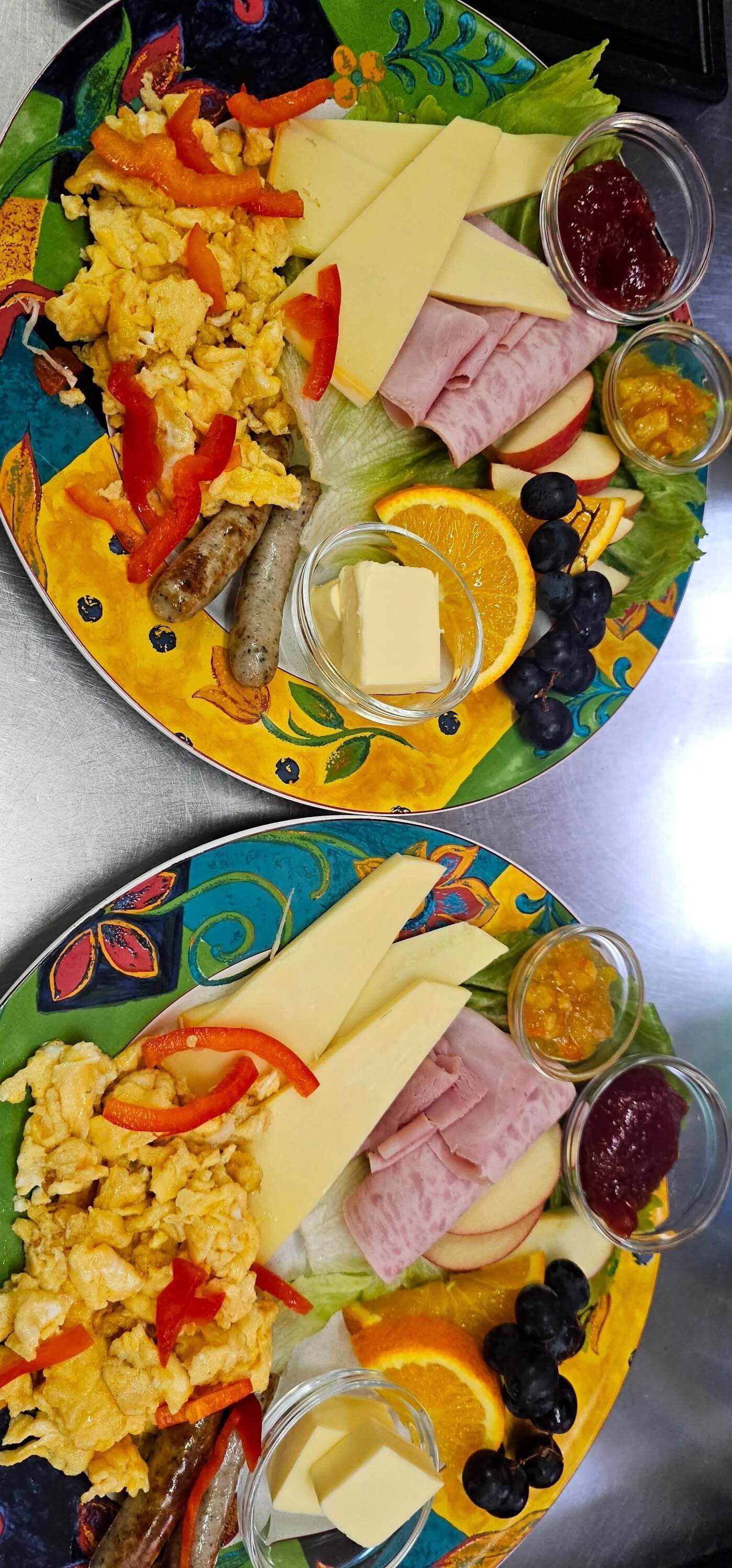 A colorful plate with scrambled eggs, ham, cheese, and various fruits and vegetables.