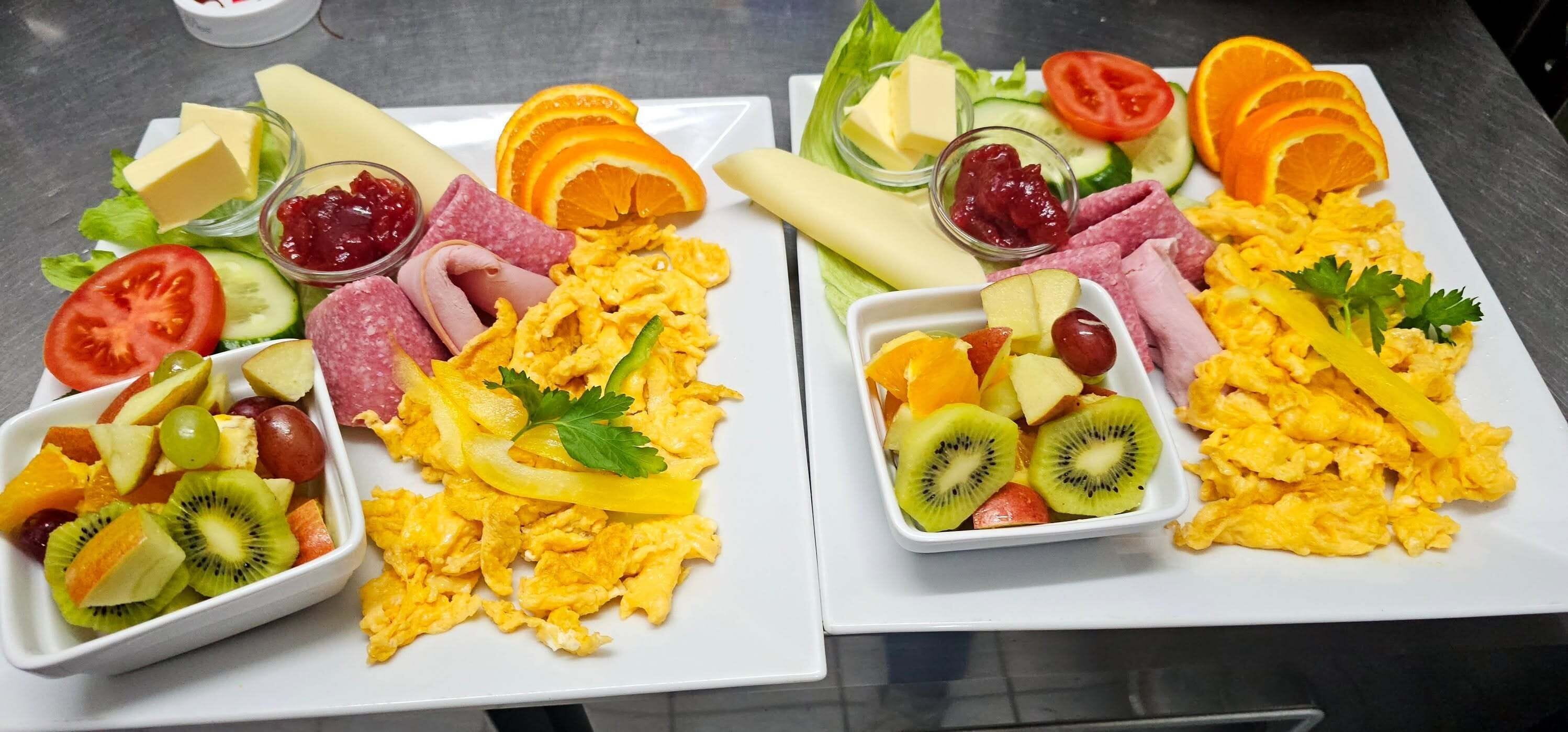 Two plates of scrambled eggs with various accompaniments including cheese, ham, and fruit.
