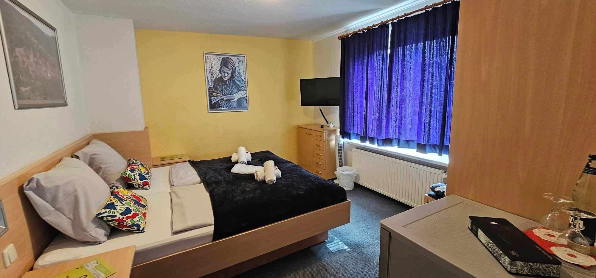Een hotelkamer met een bed, bureau, raam met gordijnen, radiator en televisie.