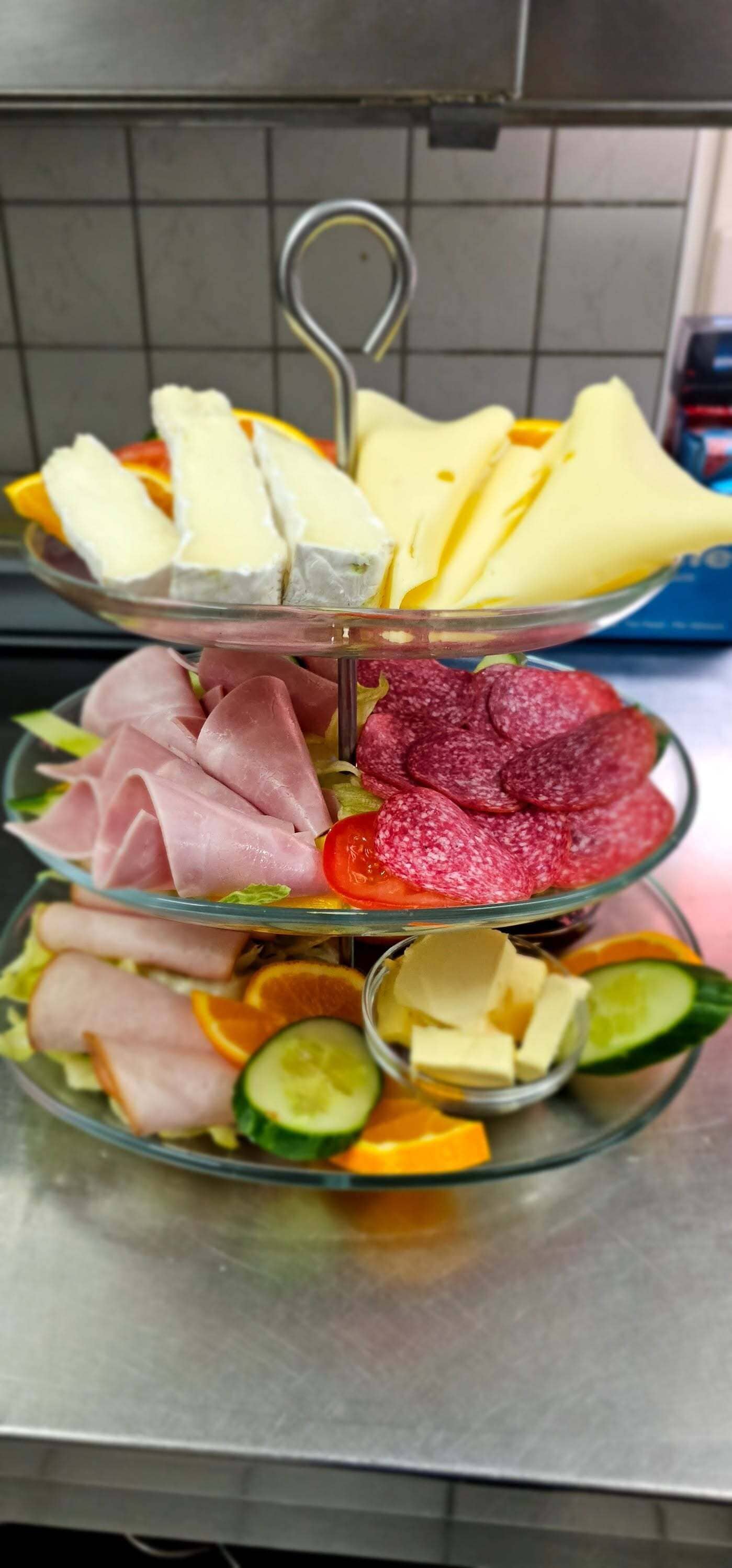 A multi-tiered glass platter with various food items including cheese, cured meats, and vegetables.