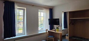 A hotel room with two windows, a desk with a television, a chair, and a wardrobe. - Tropicana Lüneburger Hof (Munster im Heidekreis)